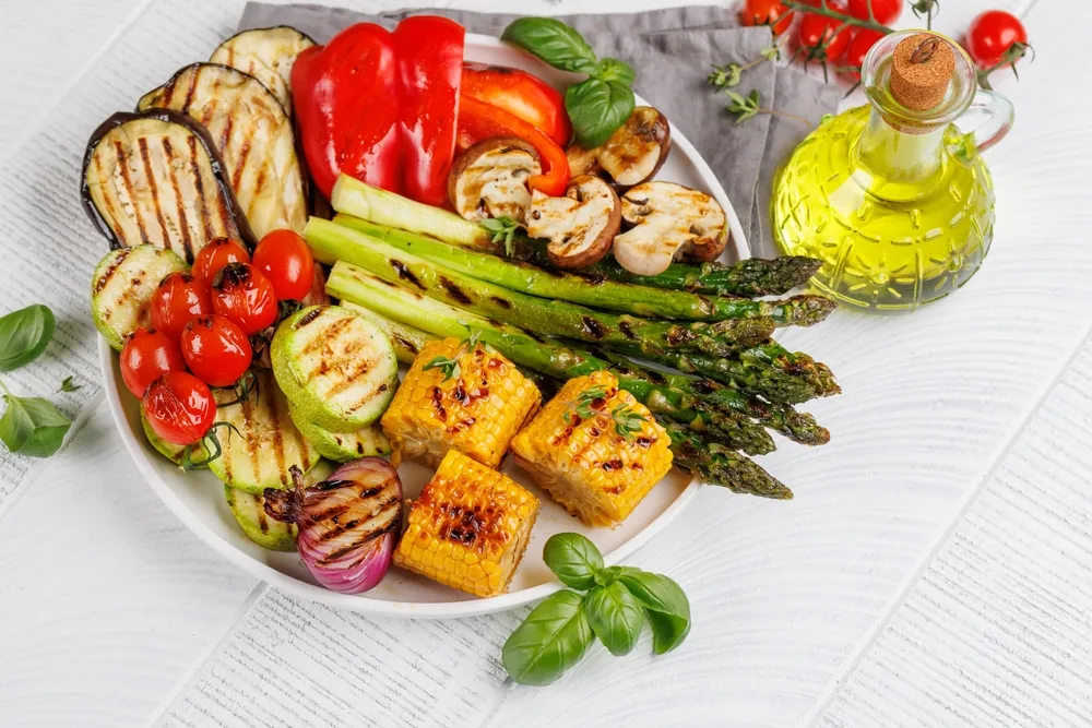 Platter of assorted grilled vegetables including asparagus, corn, zucchini, and peppers, served with olive oil.