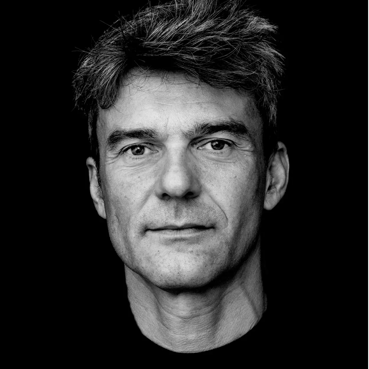 Ritratto in bianco e nero di uomo adulto in primo piano, espressione calma e lineamenti marcati su sfondo completamente nero.