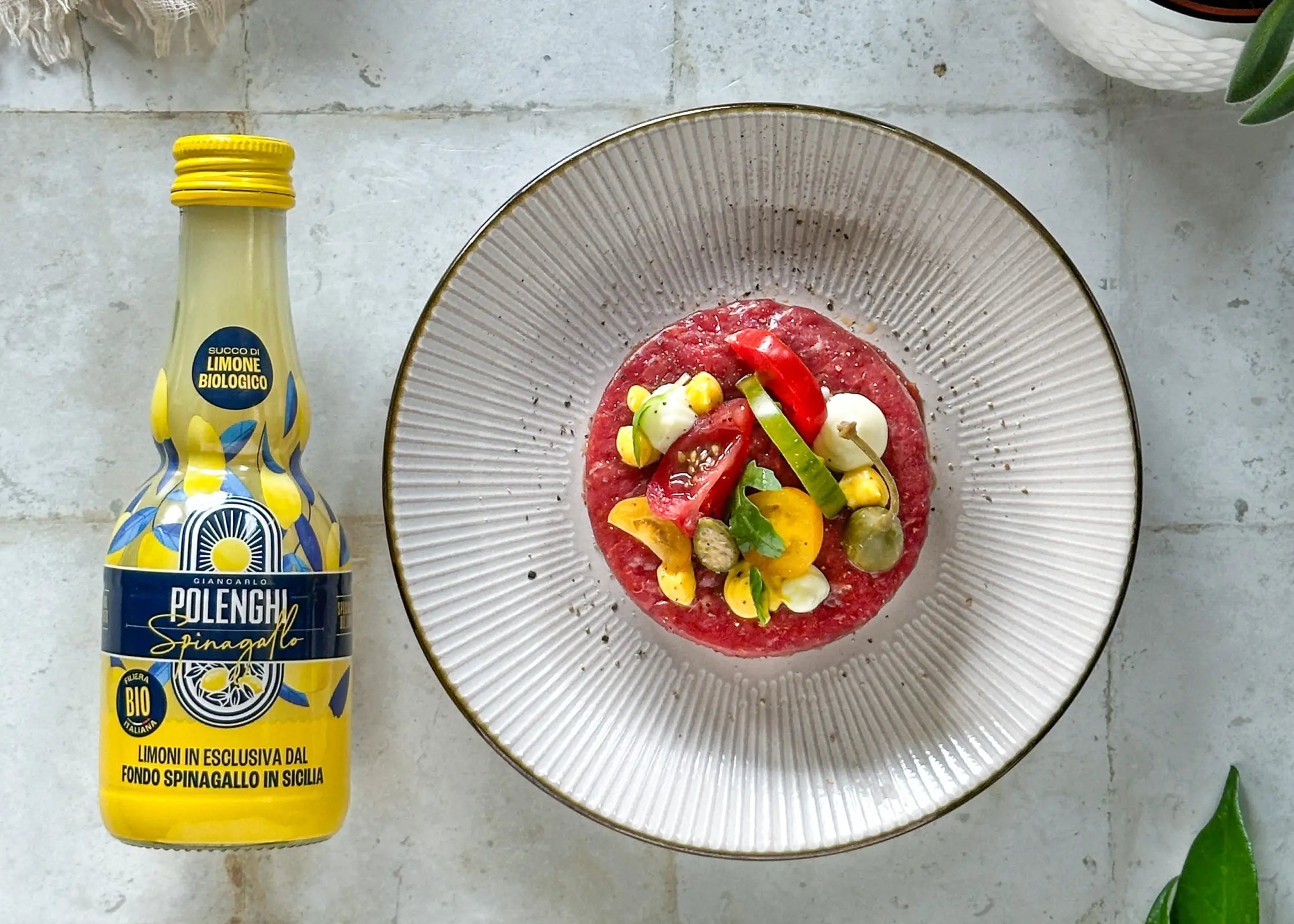 Bottiglia di succo di limone Giancarlo Polenghi a sinistra e piatto elegante con tartare colorata e verdure su piatto in ceramica