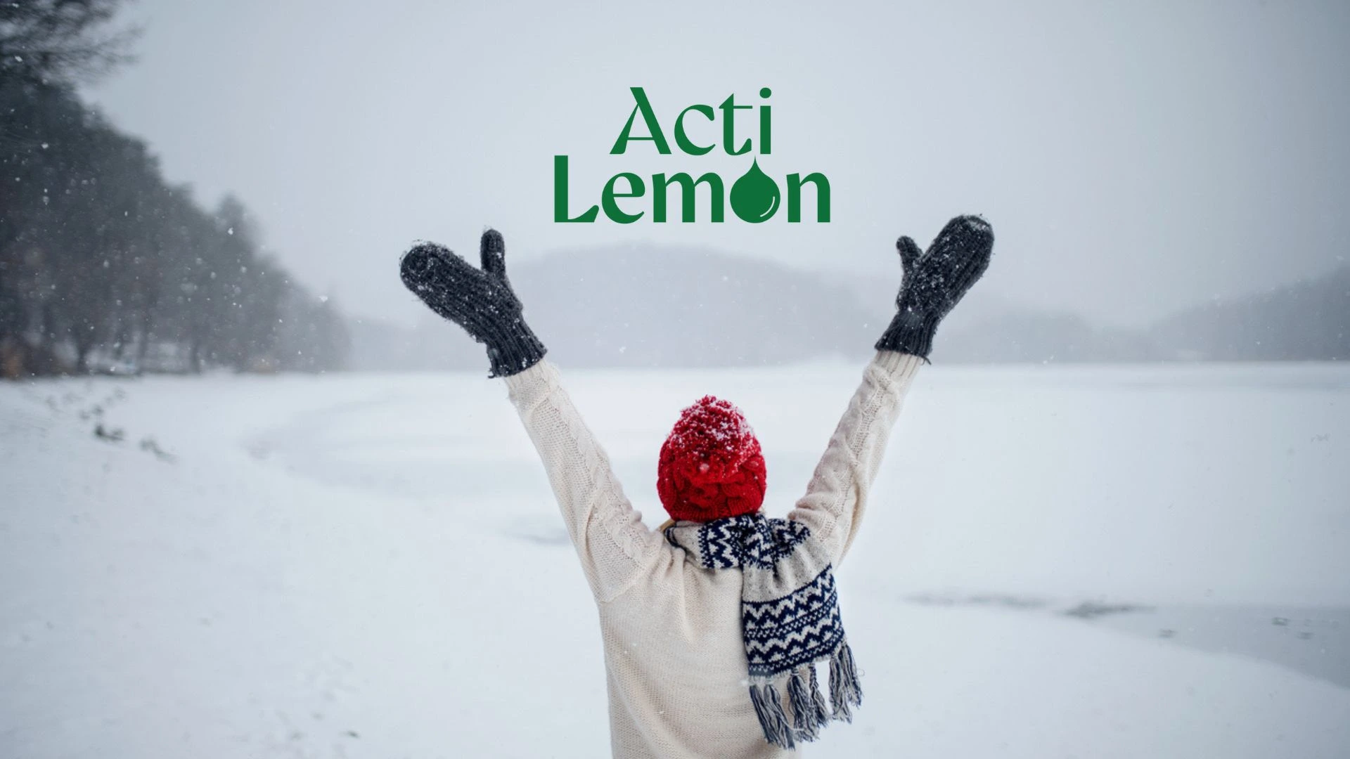 Una persona in abiti invernali è in piedi con le braccia alzate in un paesaggio innevato, di spalle alla telecamera. La neve ricopre il terreno e gli alberi. Sopra la persona sono visibili le parole “Acti Lemon”.