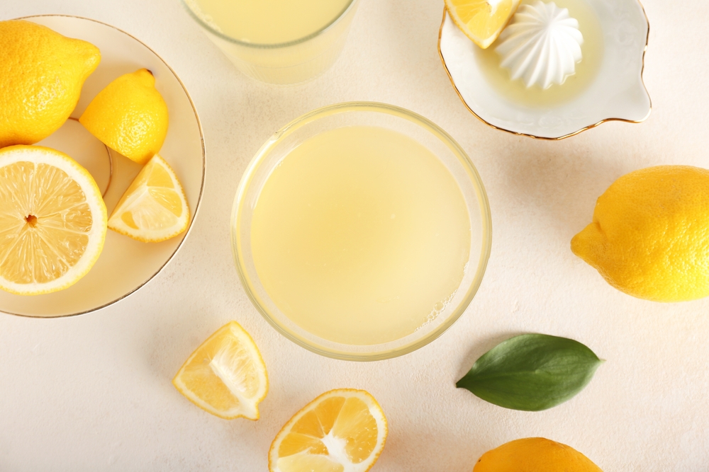 A glass bowl full of lemon juice, surrounded by fresh lemons, lemon wedges and a lemon squeezer.