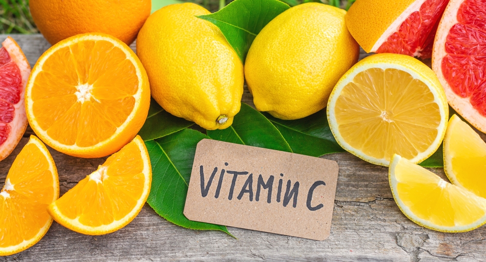 Una varietà di agrumi freschi, tra cui arance, limoni e pompelmi, disposti attorno a un cartellino con la scritta VITAMINA C.